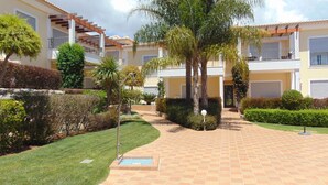 A courtyard with a tiled walkway, palm trees, and a building with balconies.