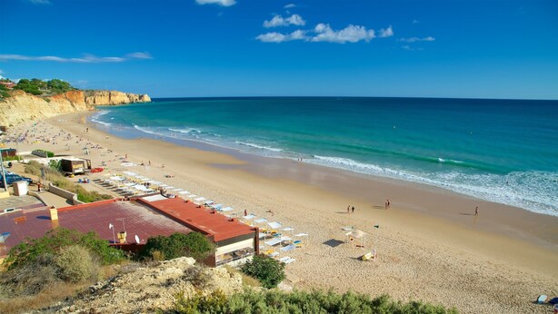 A beach with a long stretch of sand, a few umbrellas, and a building with a red roof.