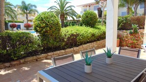 A patio with a table and chairs, surrounded by a well-maintained hedge and a stone wall.