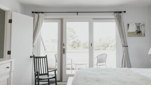 A bedroom with a bed, a chair, a balcony with chairs, and a view of the outdoors. - Sunset Villa Across the Street from Beach & Walk to Pool / Golf
 (Johns Island)