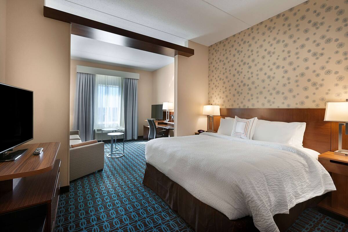 A hotel room with a large bed, a desk with a chair, a TV, and a window with curtains.