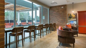 Un espace de détente intérieur moderne, avec un mélange de sièges de style bar et de fauteuils confortables, de grandes fenêtres et un mur en briques.