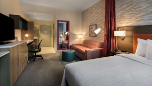 Une chambre d’hôtel avec un lit, un bureau, une chaise, une télévision et une salle de bain visible à travers une porte ouverte.