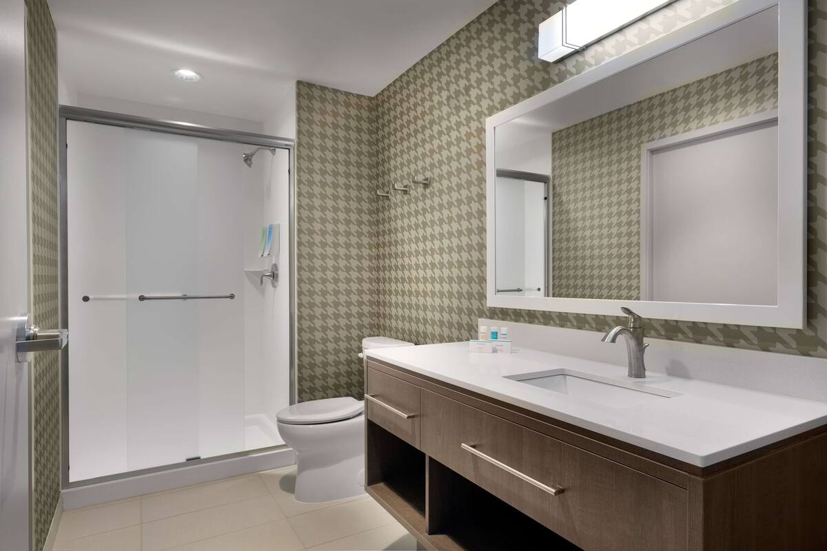 A modern bathroom with a shower, toilet, and vanity with a large mirror.