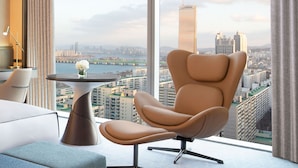 Een moderne hotelkamer met een groot raam met uitzicht op de stad, een comfortabele fauteuil, een klein tafeltje met een vaas en een lamp.