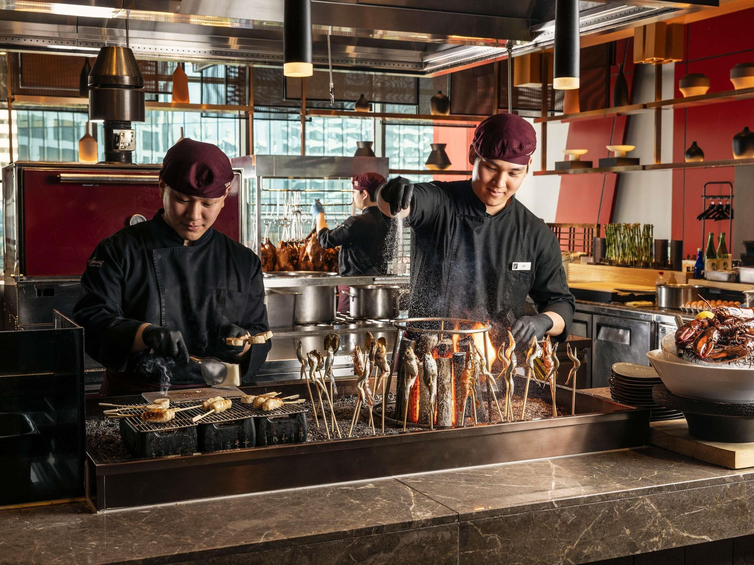 Des chefs préparent des plats de fruits de mer dans une cuisine professionnelle équipée d’appareils en acier inoxydable et dotée d’un plan de travail en marbre.