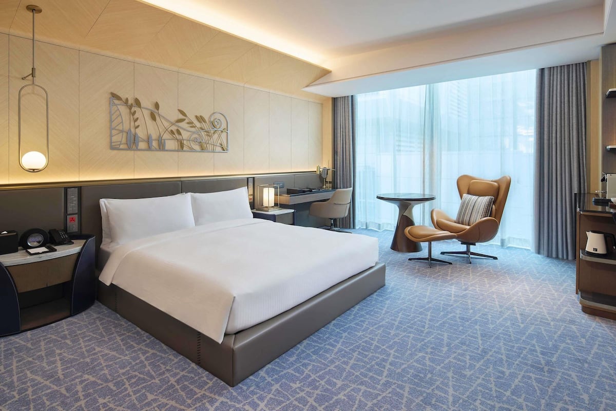Une chambre d’hôtel moderne avec un grand lit, un bureau, une chaise et une grande fenêtre avec des rideaux.