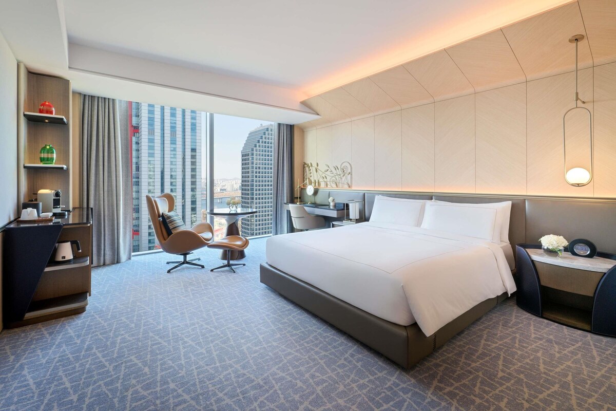 Une chambre d’hôtel moderne, dotée d’un grand lit, d’un bureau, d’une chaise et offrant une vue sur le paysage urbain.