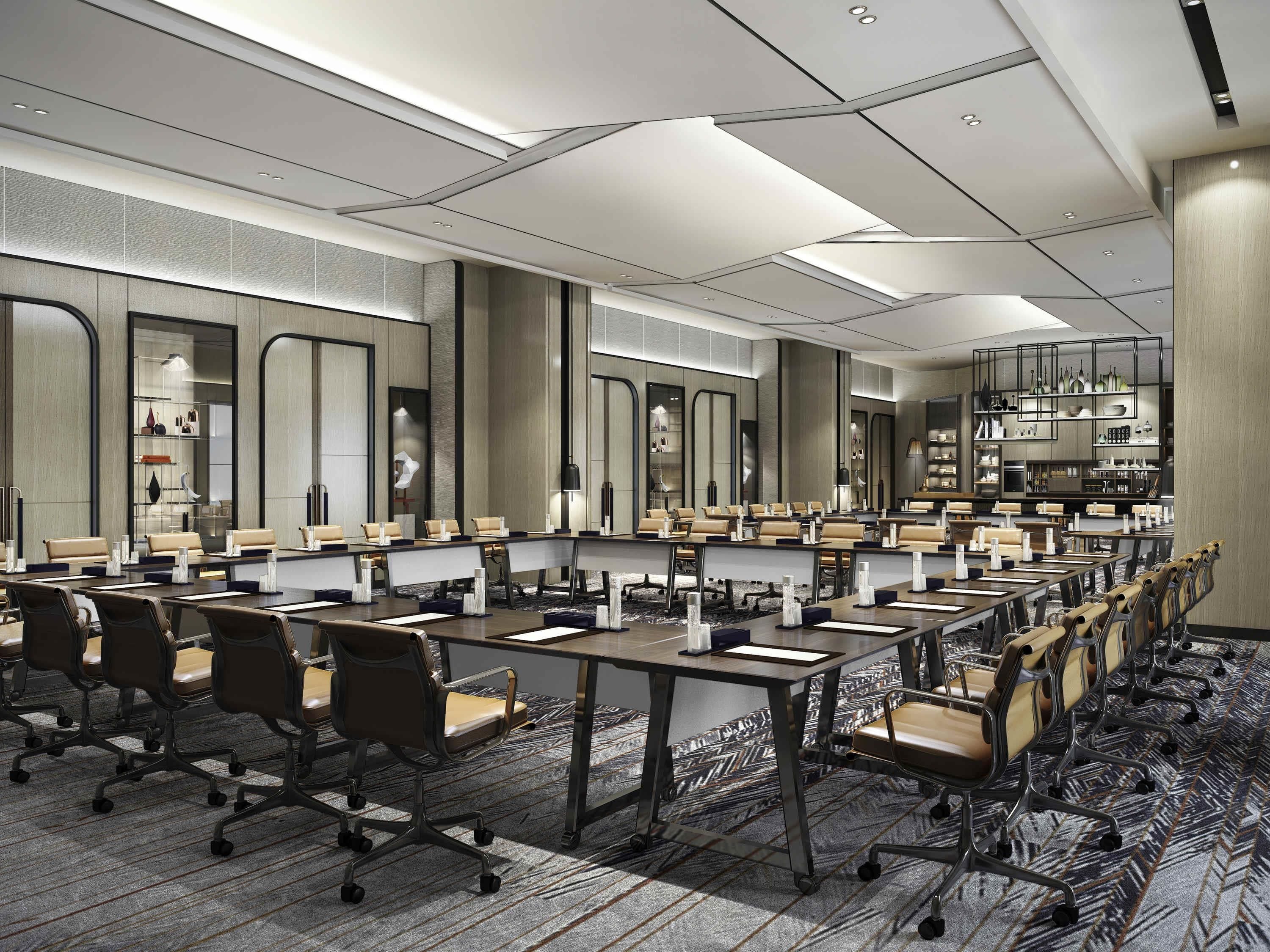 A modern conference room with multiple tables and chairs, large windows, and a kitchen area visible through the glass.