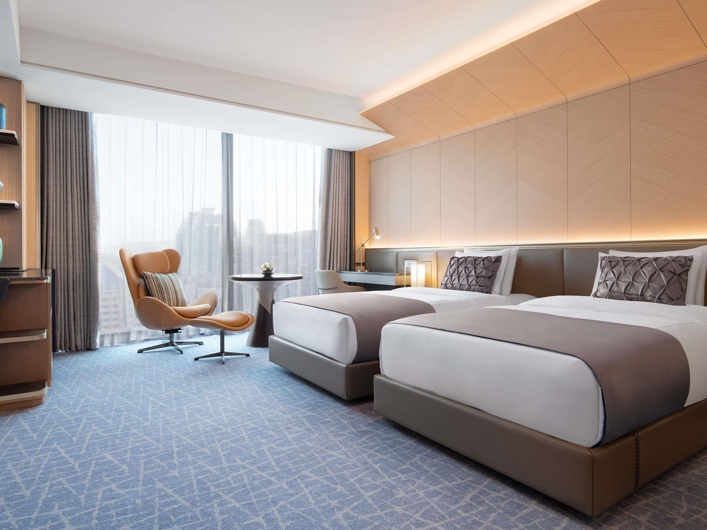 A hotel room with a large bed, a chair, a desk, and a view of the city.