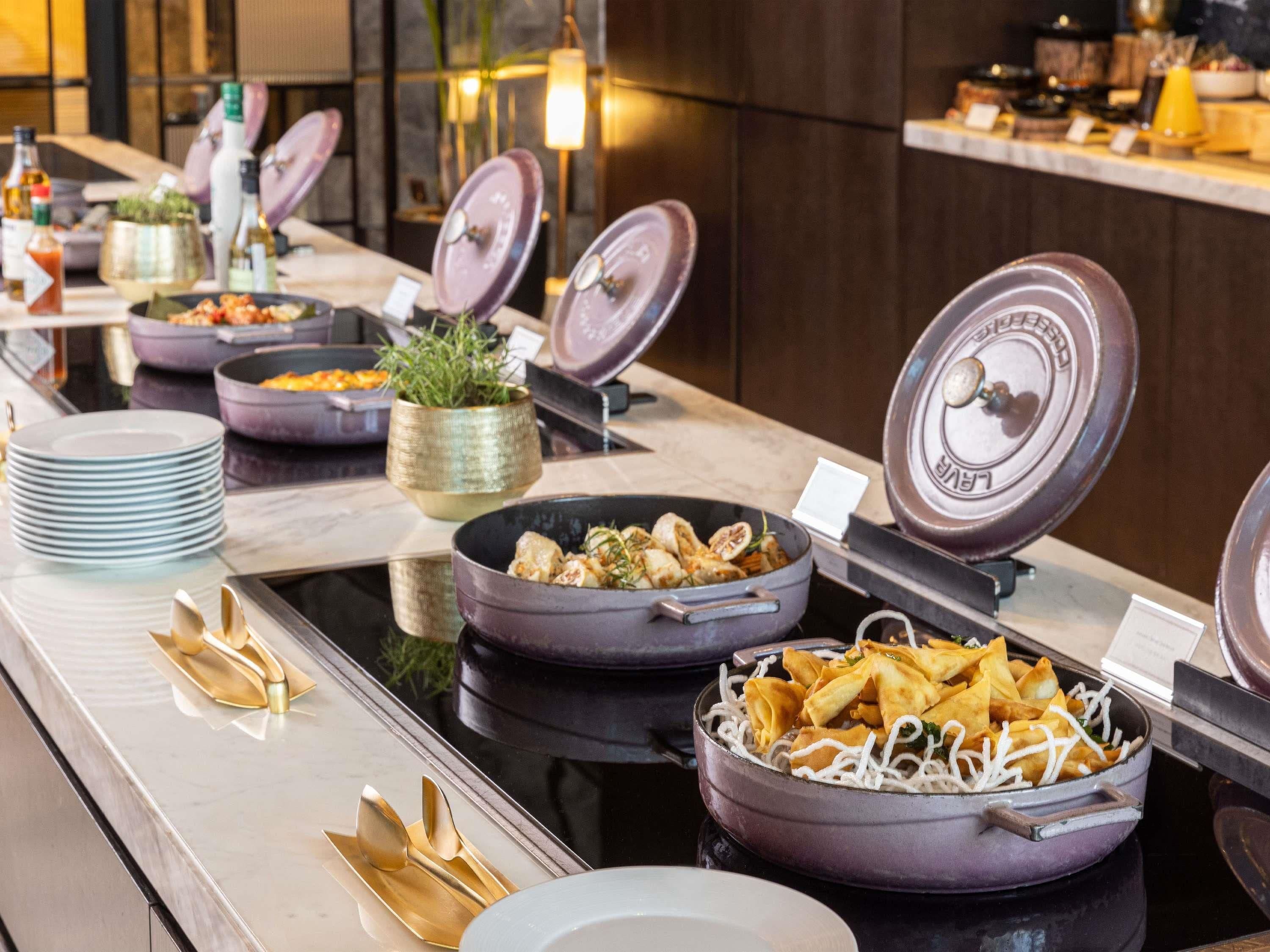 A buffet setup with various dishes, including a bowl of dumplings and a bowl of noodles, on a marble counter.