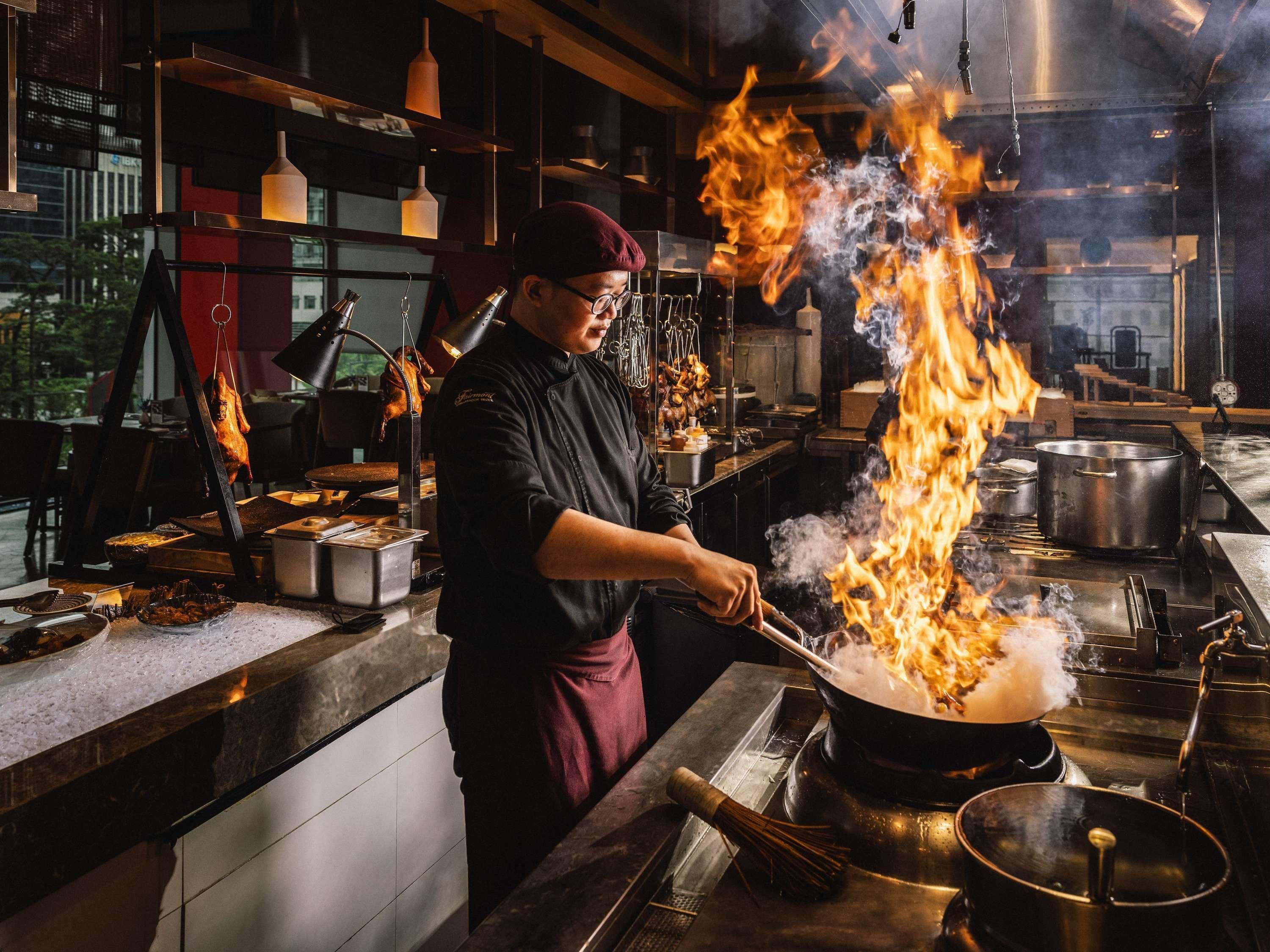 Un chef cuisinant avec des flammes dans une cuisine professionnelle.