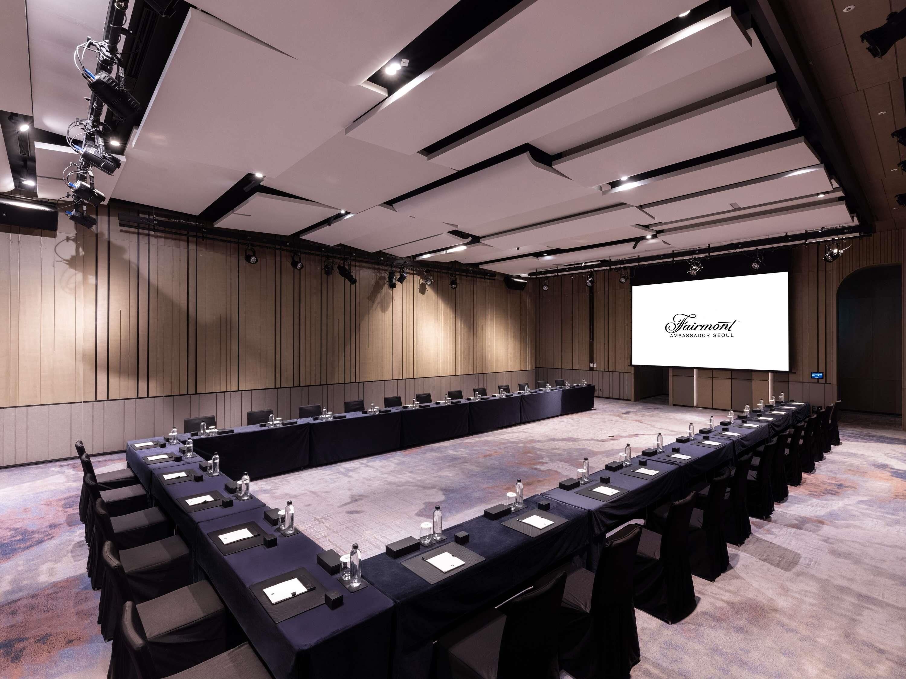 A conference room with a long table, chairs, and a large screen displaying the Fairmont name.