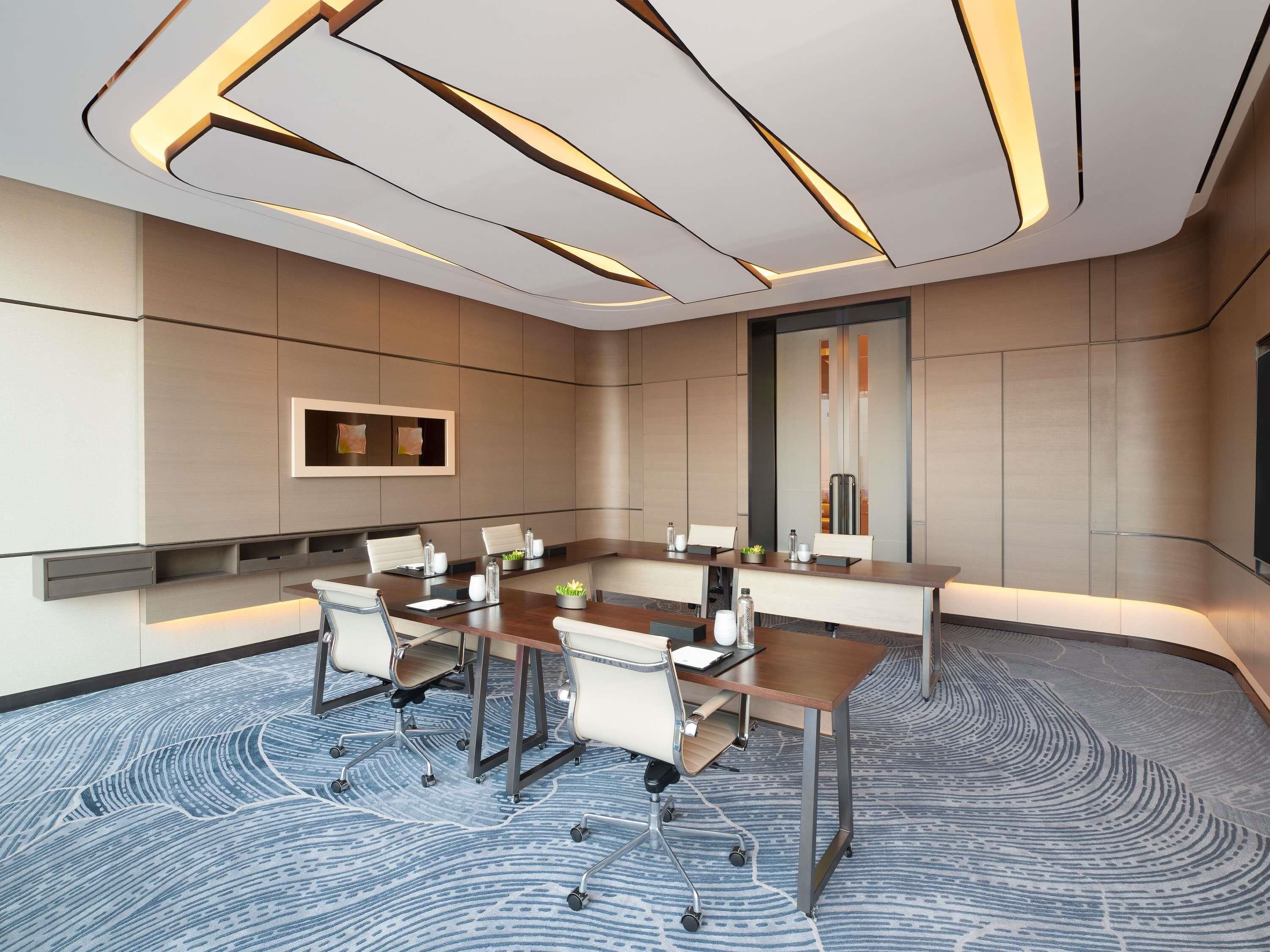A modern conference room with a long table, chairs, and a patterned carpet.
