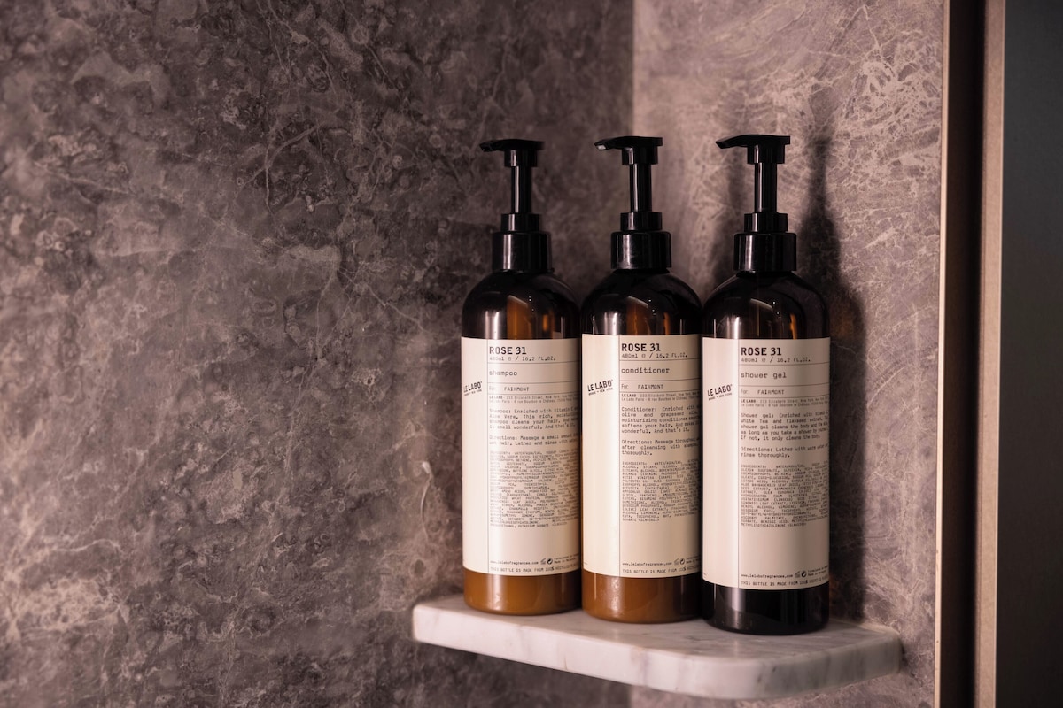 Tres botellas de champú y acondicionador Rose 31 sobre un estante de mármol.