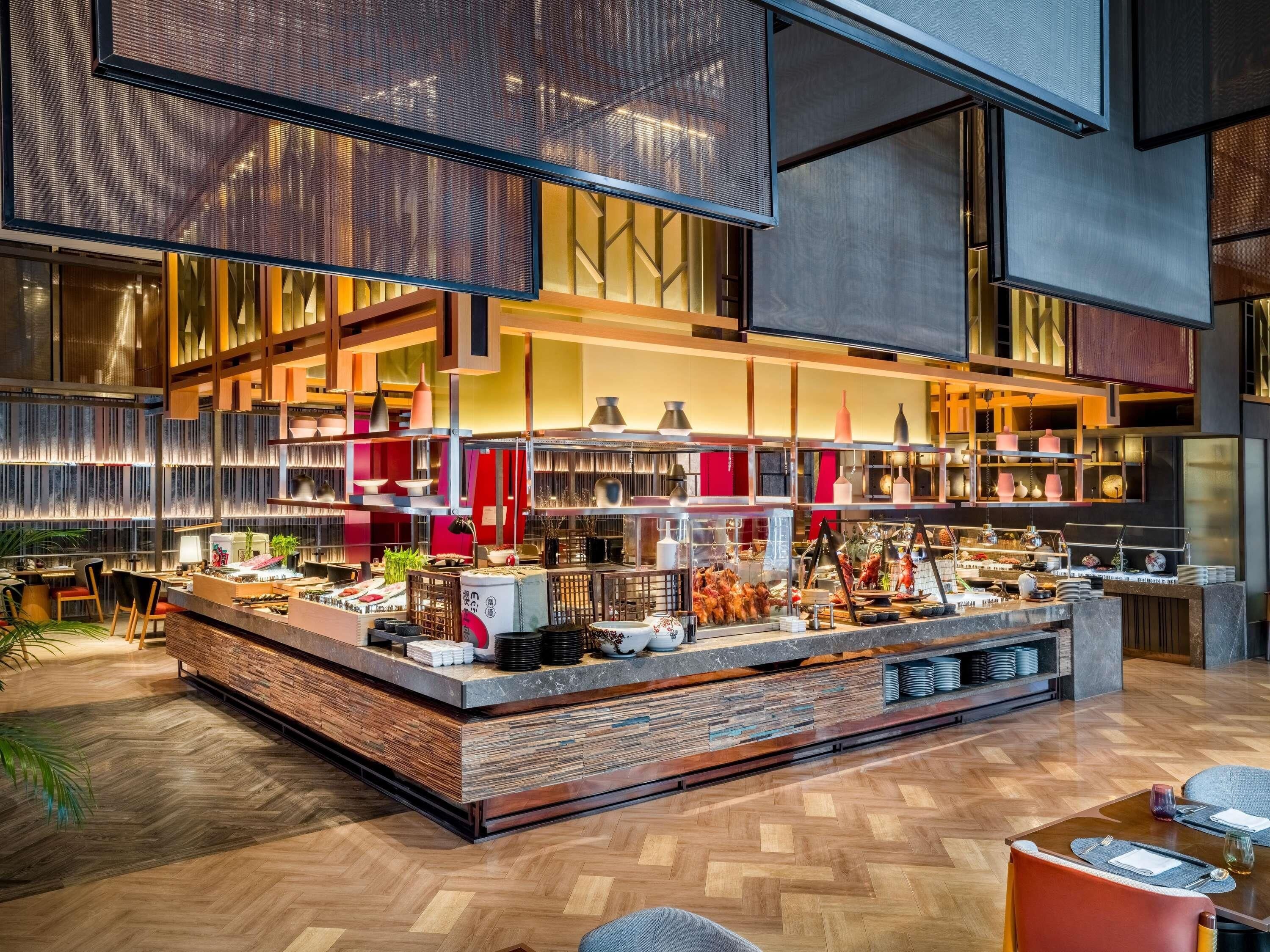 Un restaurante moderno con barra central, diferentes disposiciones de mesas y una variedad de platos exhibidos.