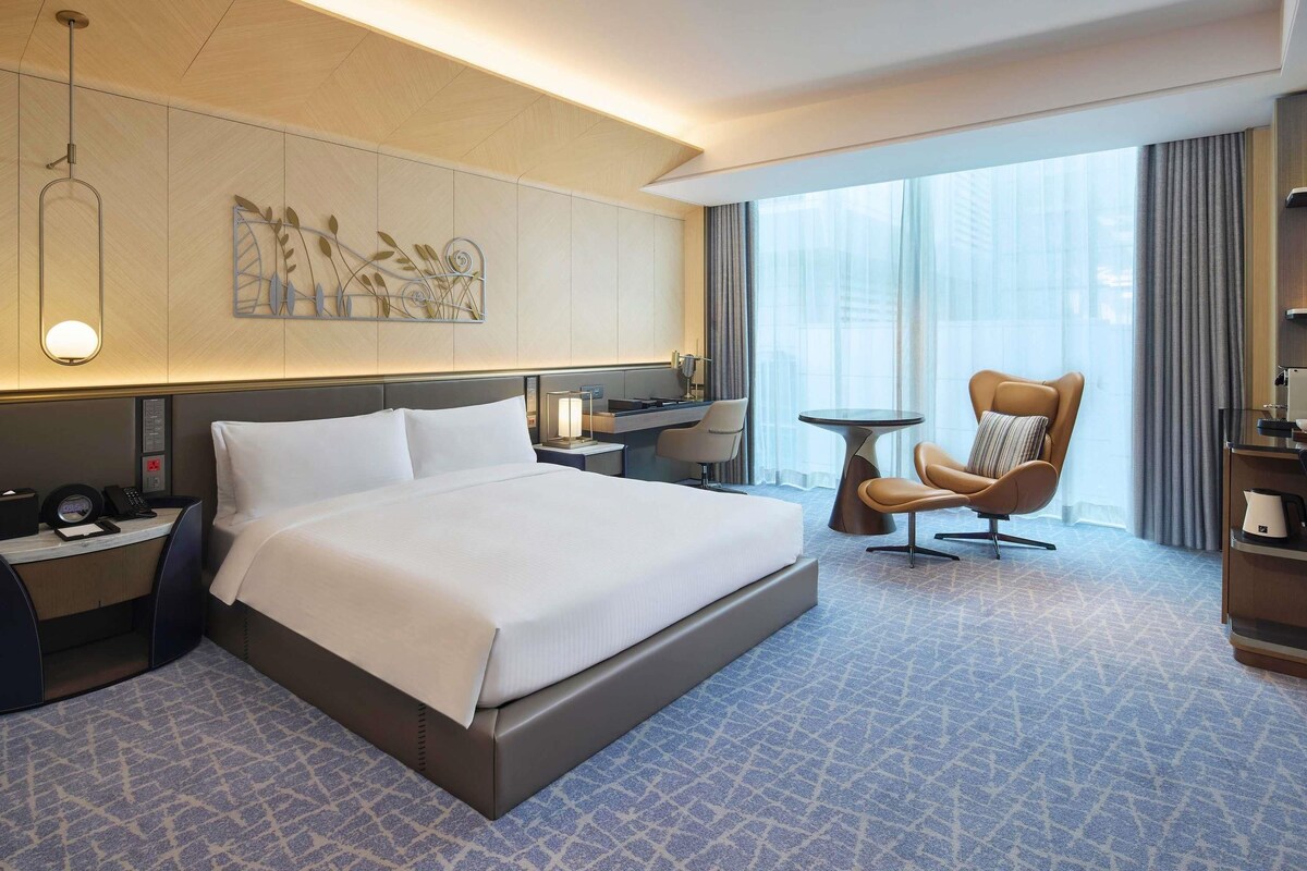 Une chambre d’hôtel moderne avec un grand lit, un bureau, une chaise et une grande fenêtre avec des rideaux.