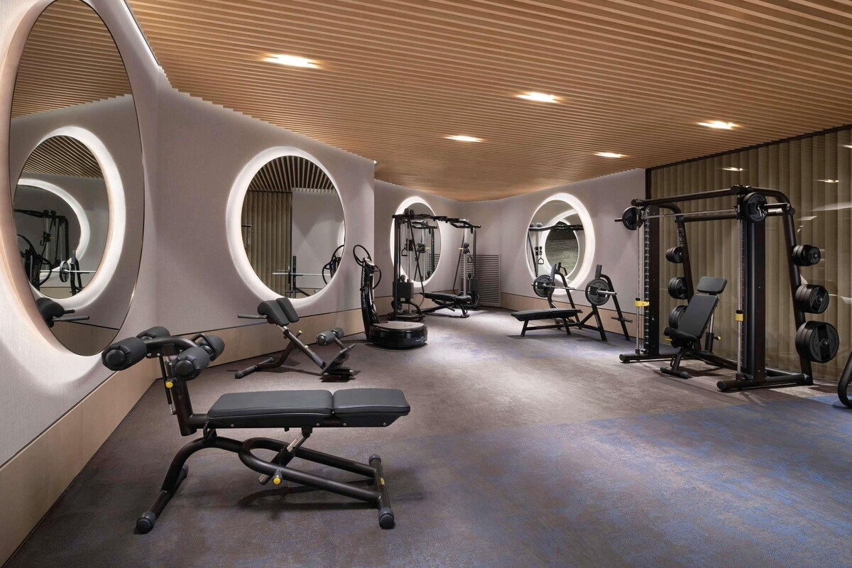 A modern gym with circular mirrors, various exercise equipment, and a bench.