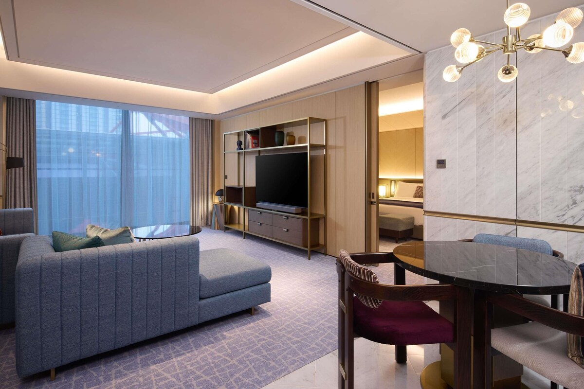 Une chambre d’hôtel moderne équipée d’un canapé, d’une table à manger, d’un téléviseur et d’un mur en marbre.