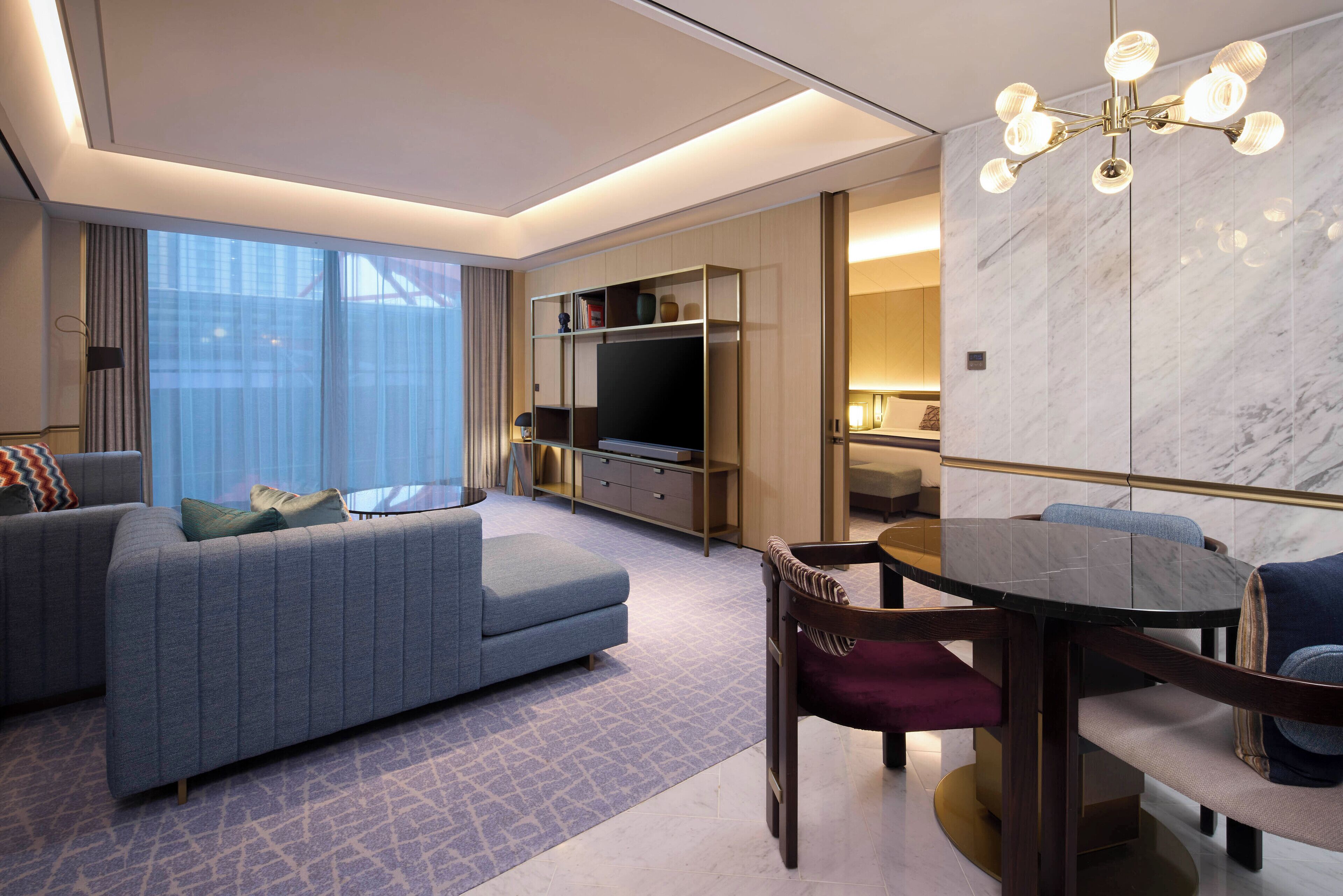 A modern hotel room with a sofa, a dining table, a TV, and a marble wall.