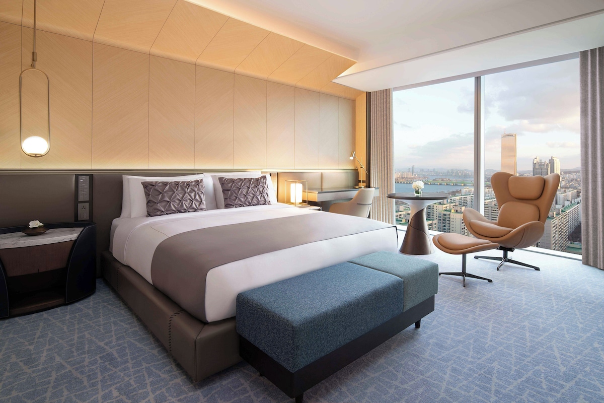 Una habitación de hotel moderna con una cama grande, una zona de estar y vistas a la ciudad.
