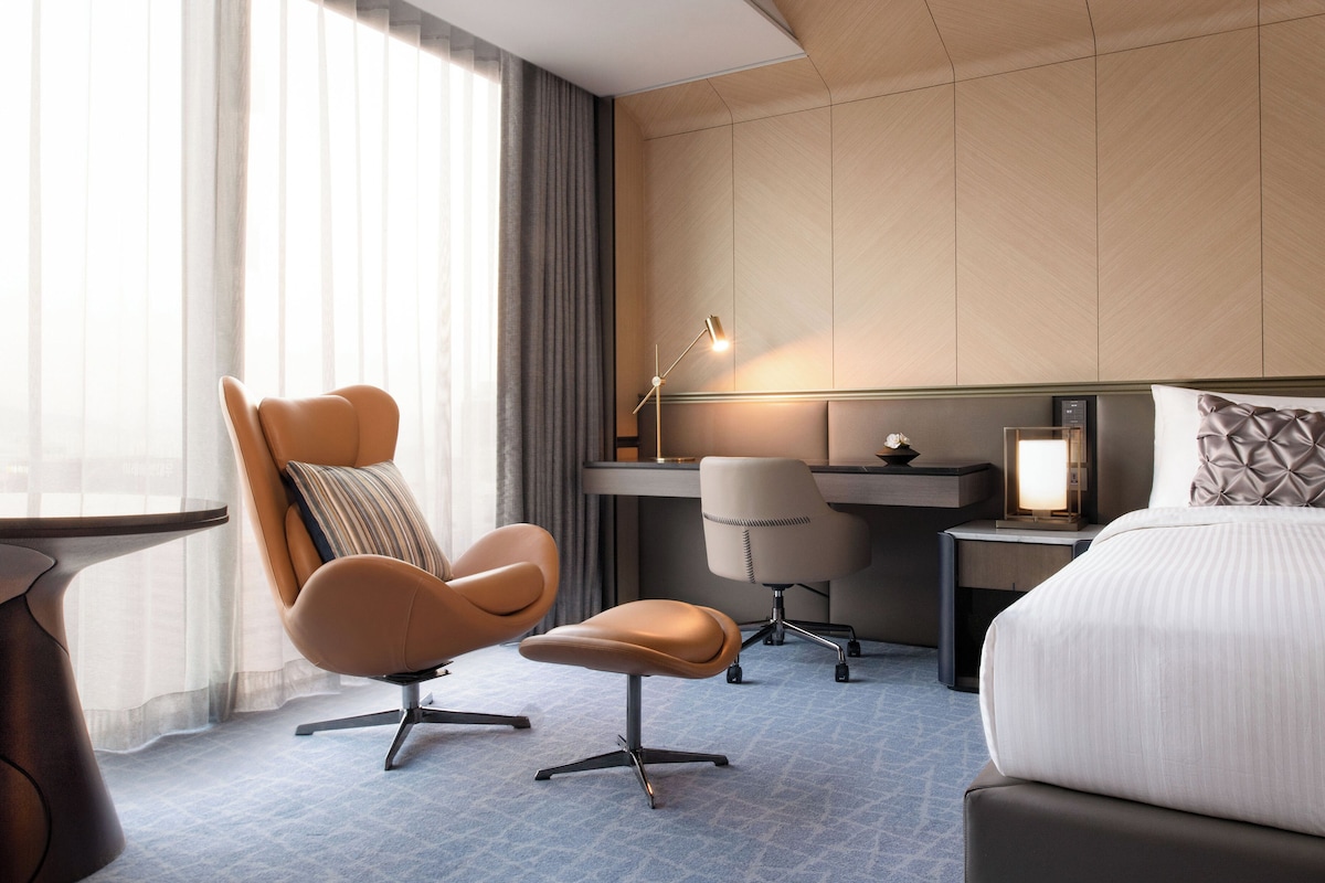 Una habitación de hotel moderna con una cama grande, un escritorio, una silla y una lámpara.