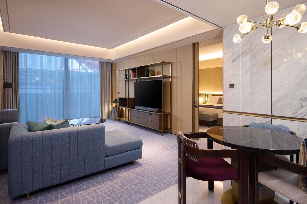 Une chambre d’hôtel moderne équipée d’un canapé, d’une table à manger, d’un téléviseur et d’un mur en marbre.