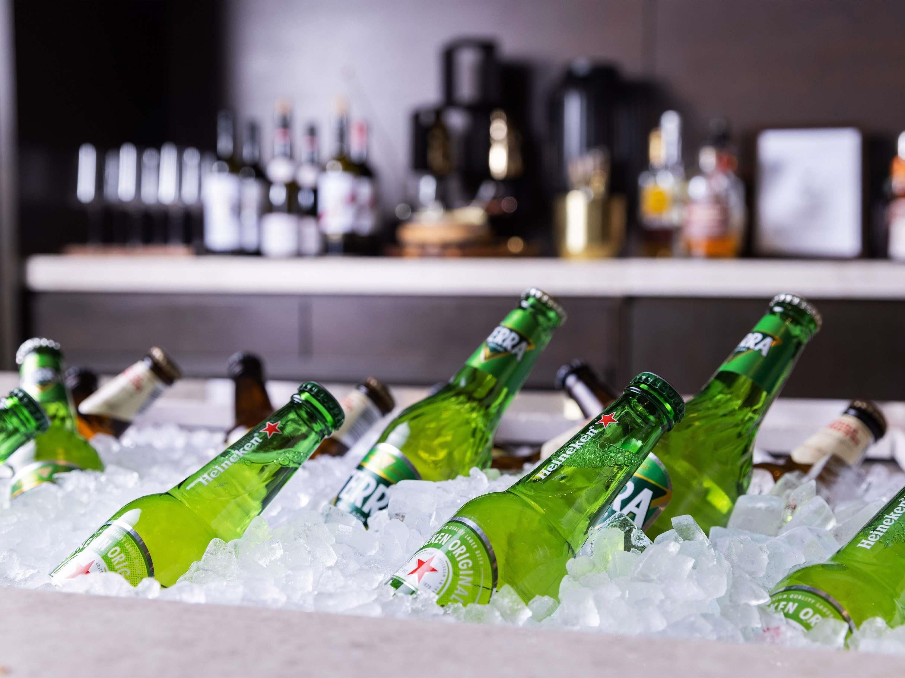 Bottles of Heineken beer in ice, with a bar and various bottles in the background.