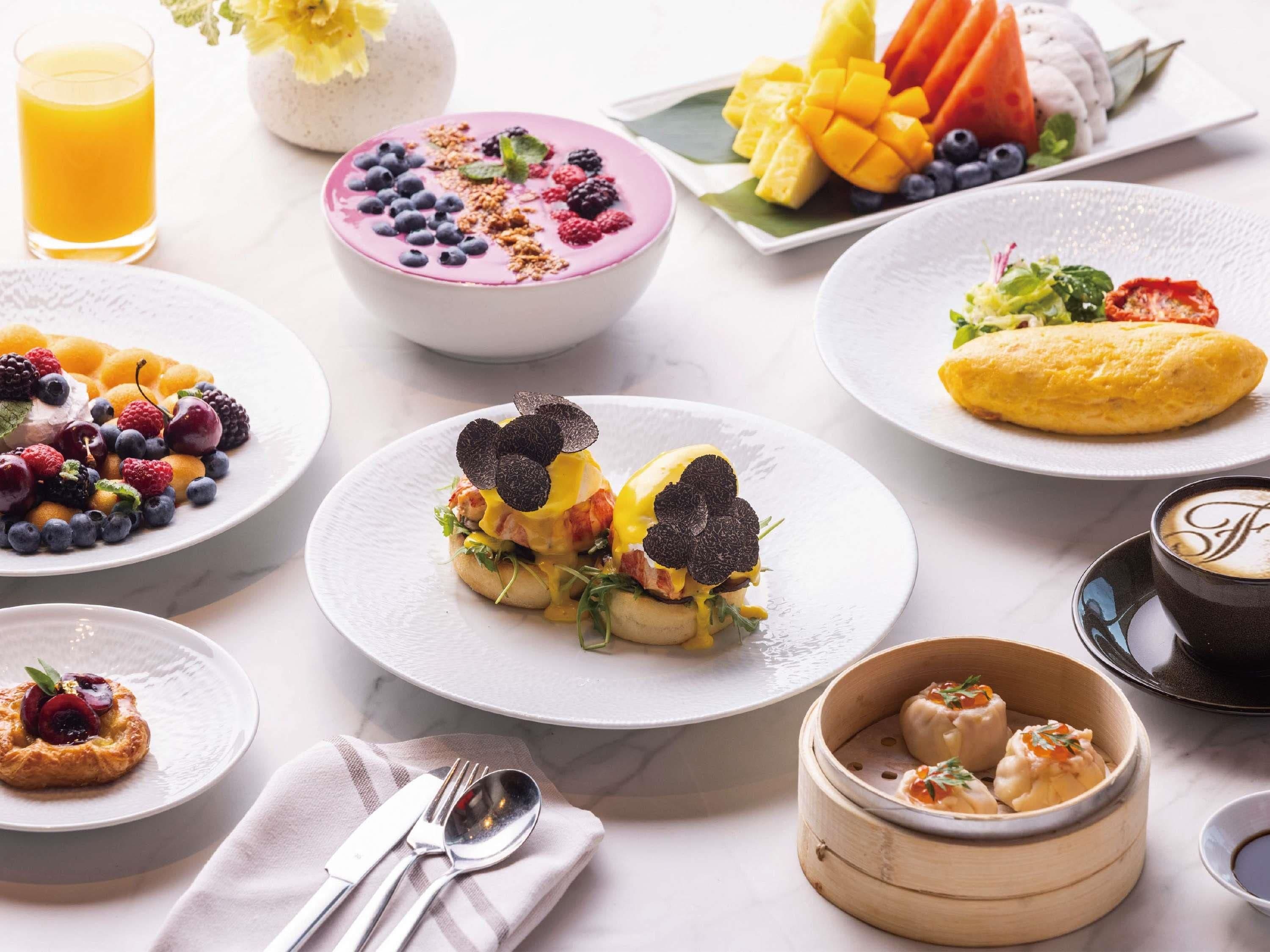 A breakfast buffet with various dishes, including eggs Benedict, fresh fruits, and a cup of coffee.