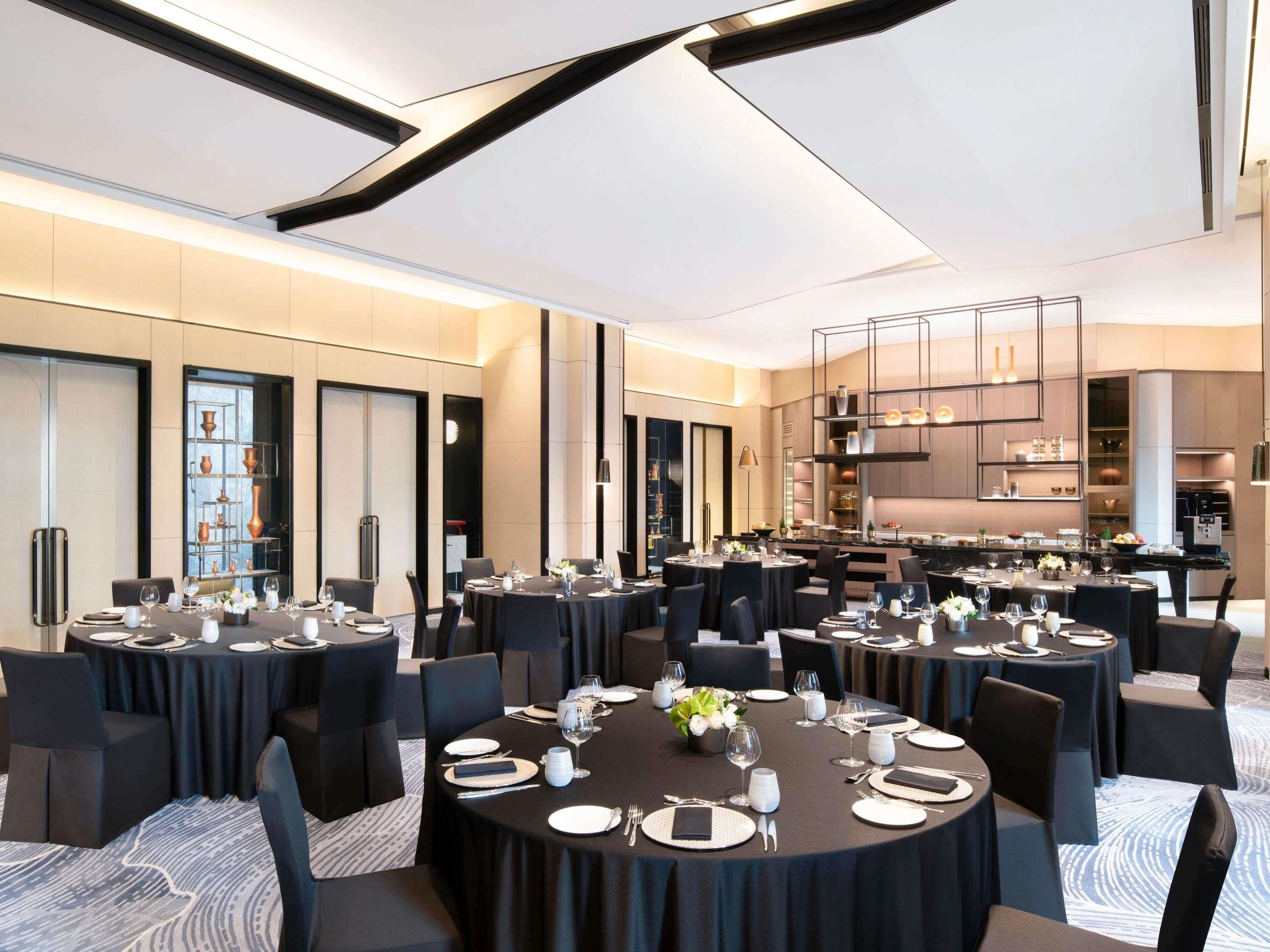 A modern dining area with multiple round tables, black tablecloths, and black chairs.