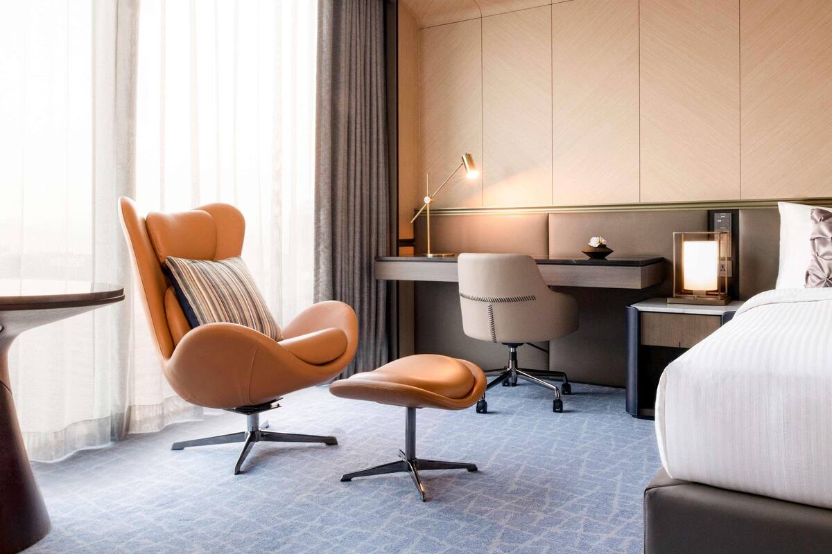 Une chambre d’hôtel avec un lit, deux chaises, un bureau, une lampe et une table de chevet.