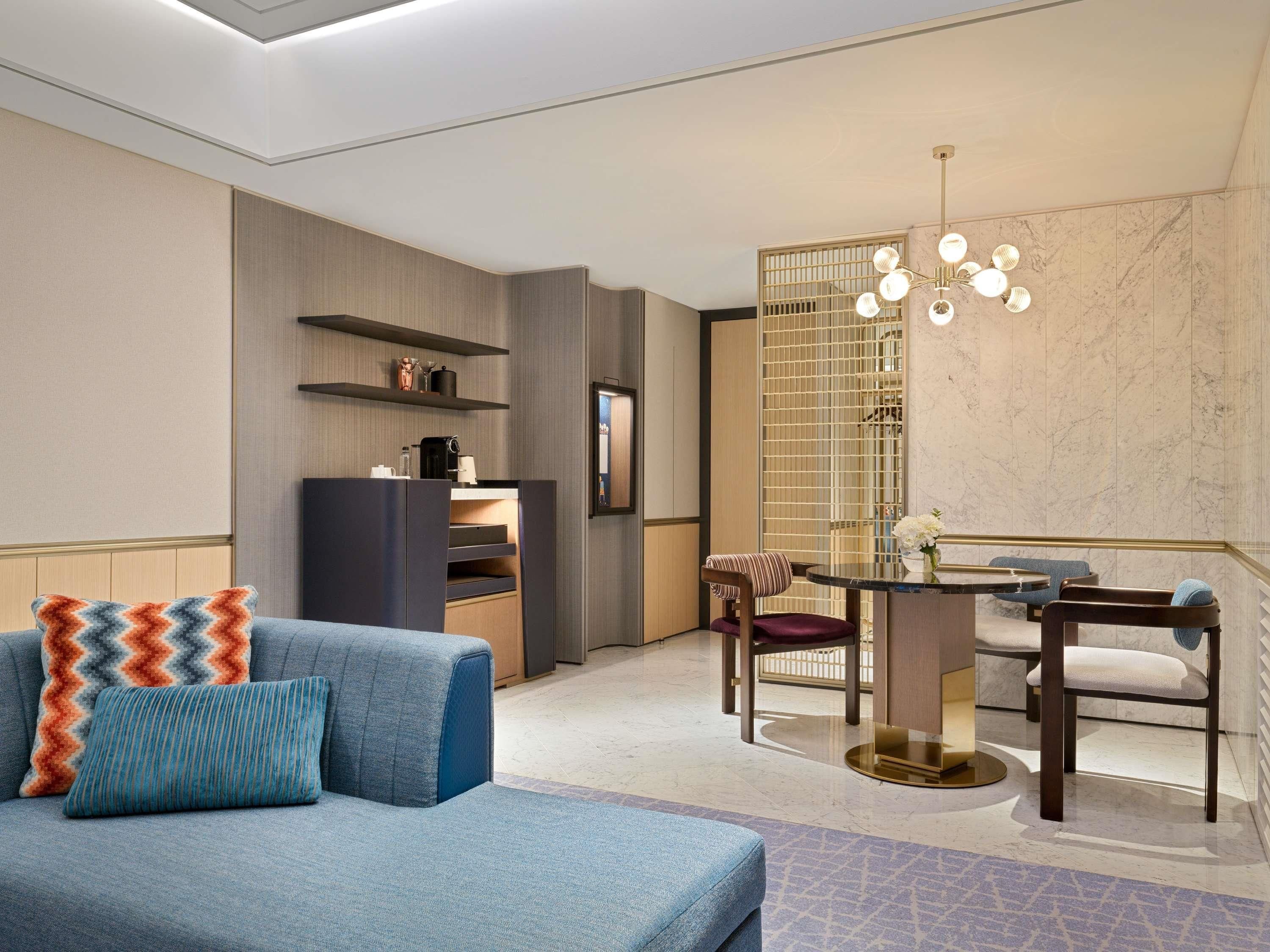A modern hotel room with a sofa, a dining table, and a chandelier.