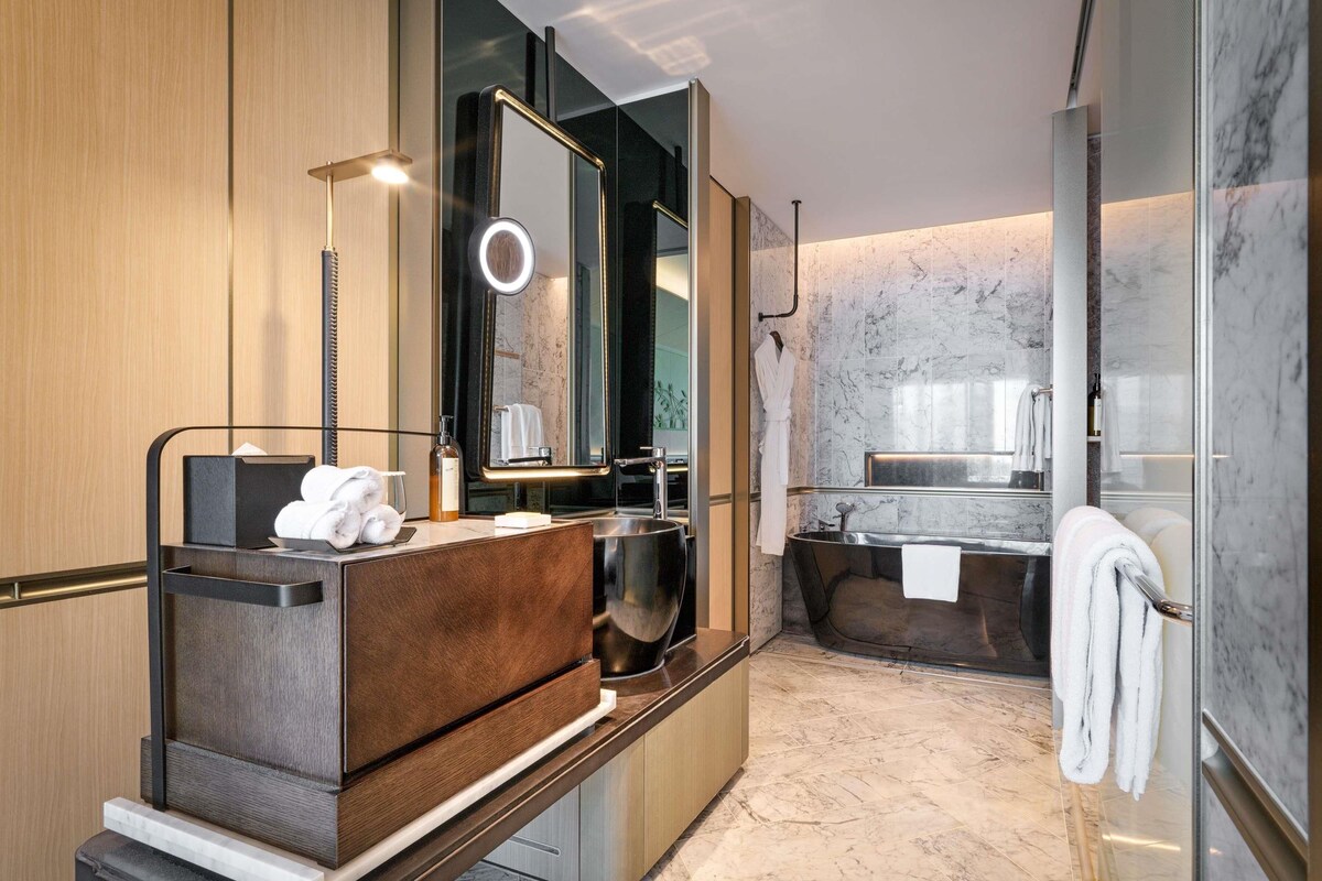Un baño moderno con un mueble de tocador de madera, un espejo grande, una lámpara redonda y una bañera independiente.
