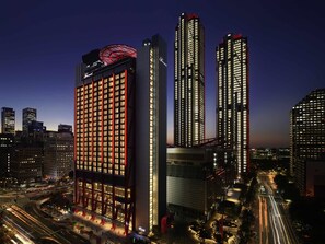 A high-rise hotel with a grid of windows, a prominent red structure on top, and a well-lit urban street below. - Fairmont Ambassador Seoul (Seoul)