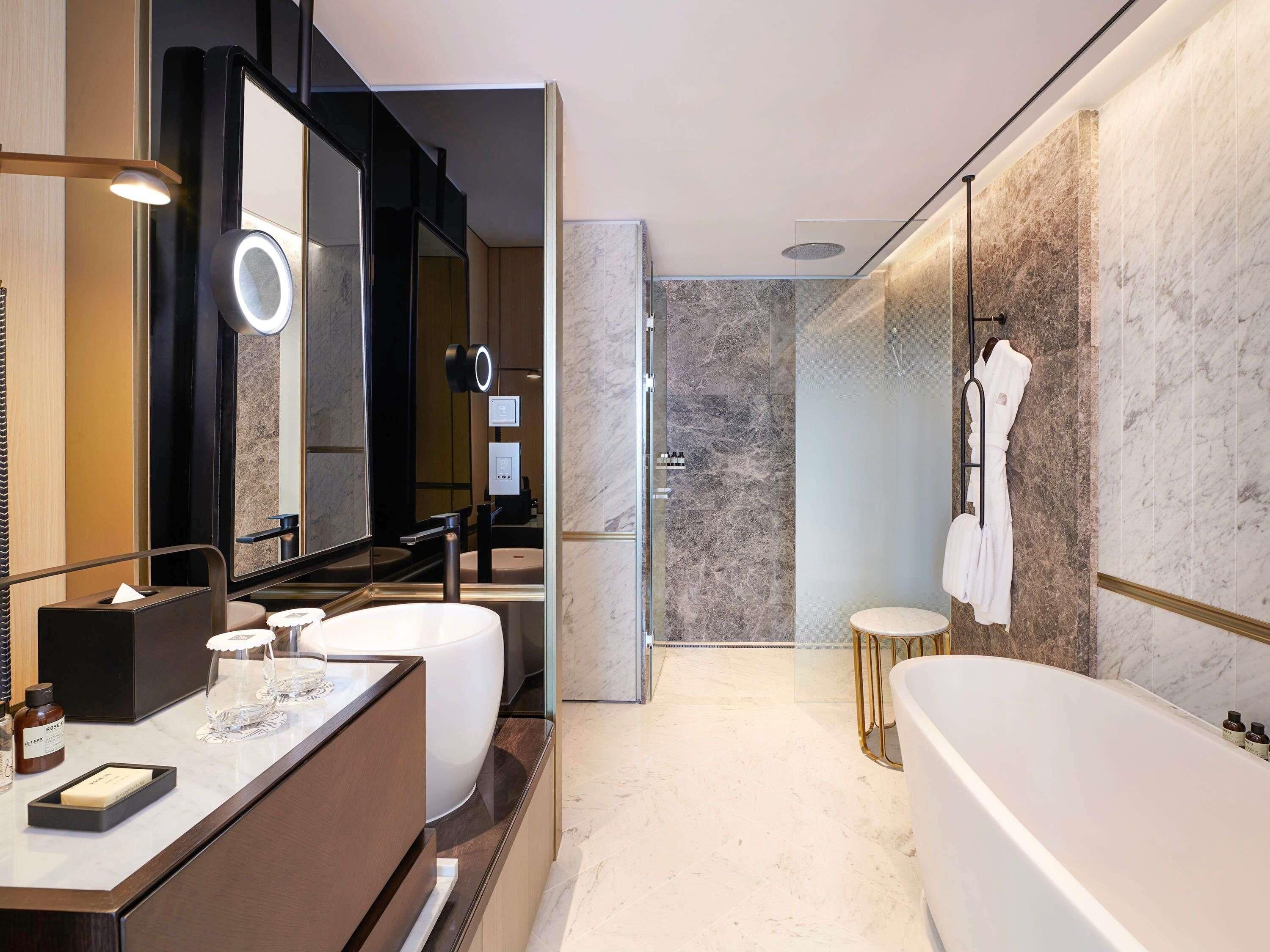 A modern bathroom with a large mirror, two sinks, a bathtub, and a glass-enclosed shower area.