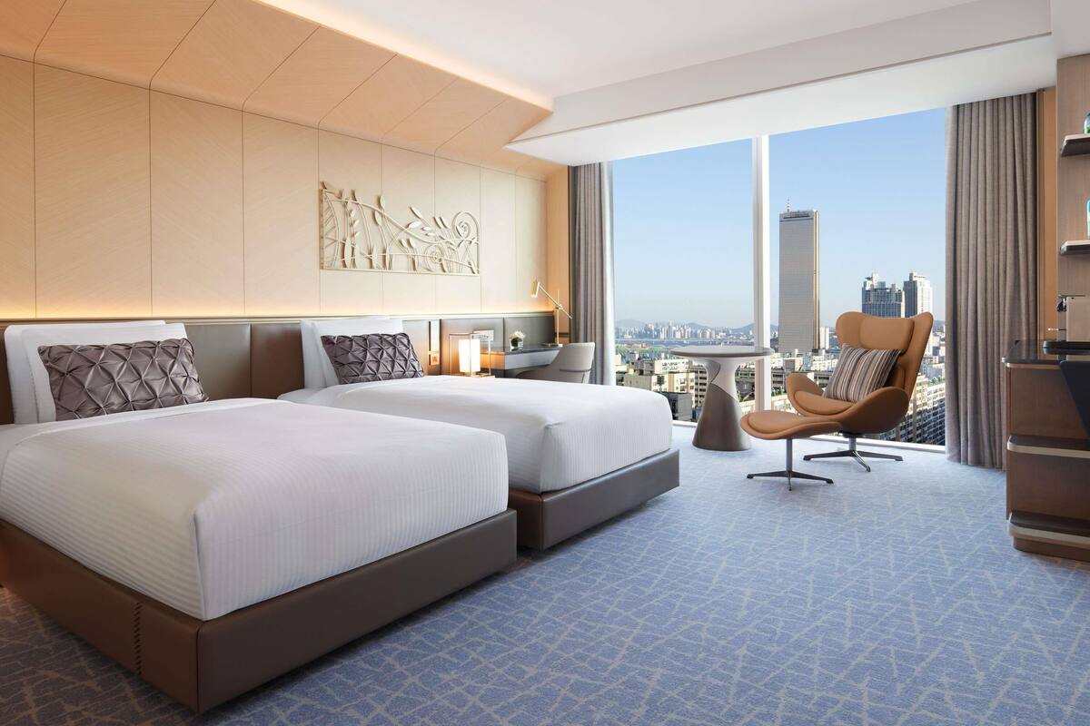 Une chambre d’hôtel avec deux lits, une vue sur la ville, un bureau et une chaise.