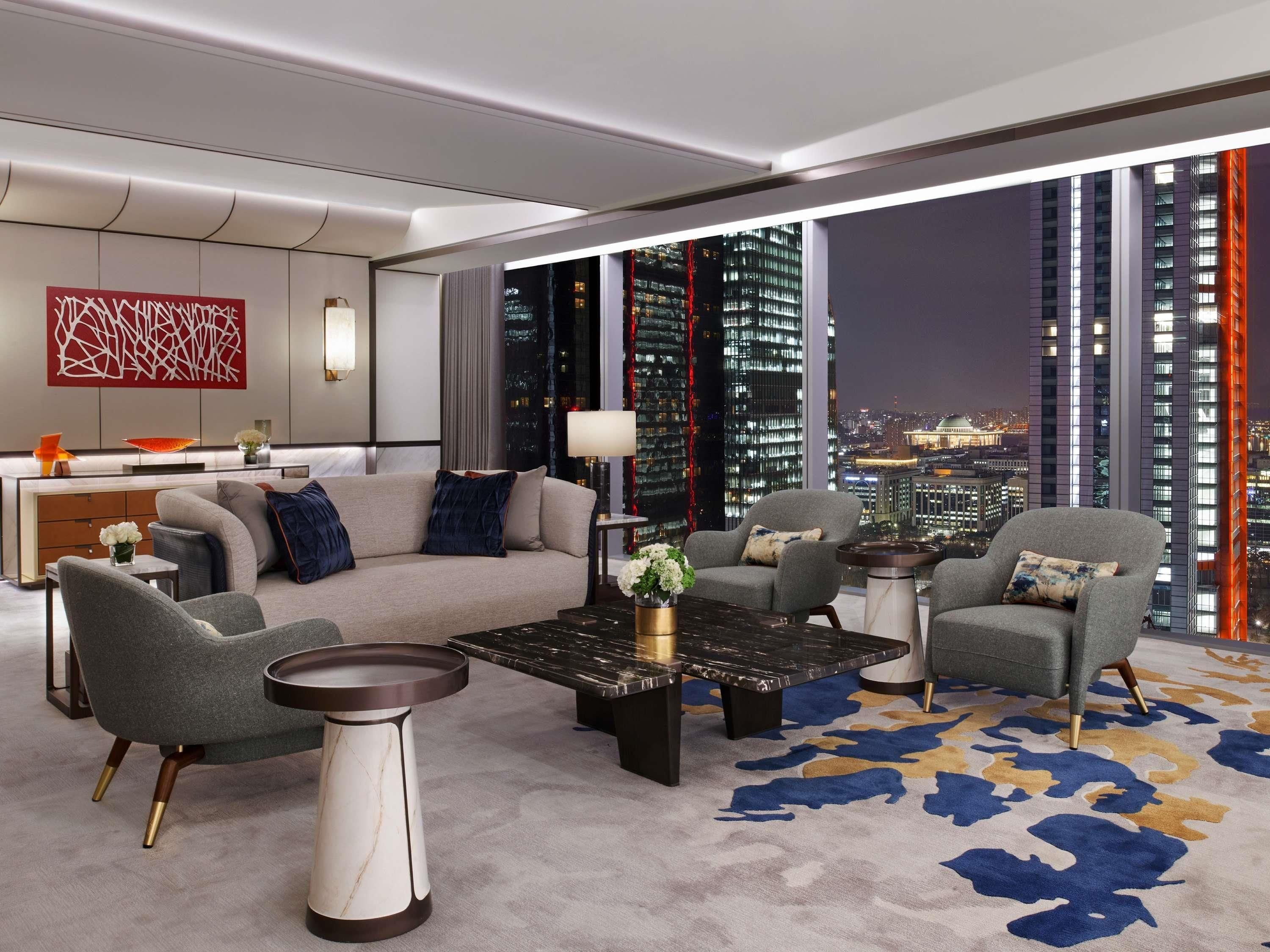 A modern living room with a sofa, armchairs, a coffee table, and a view of a cityscape at night.
