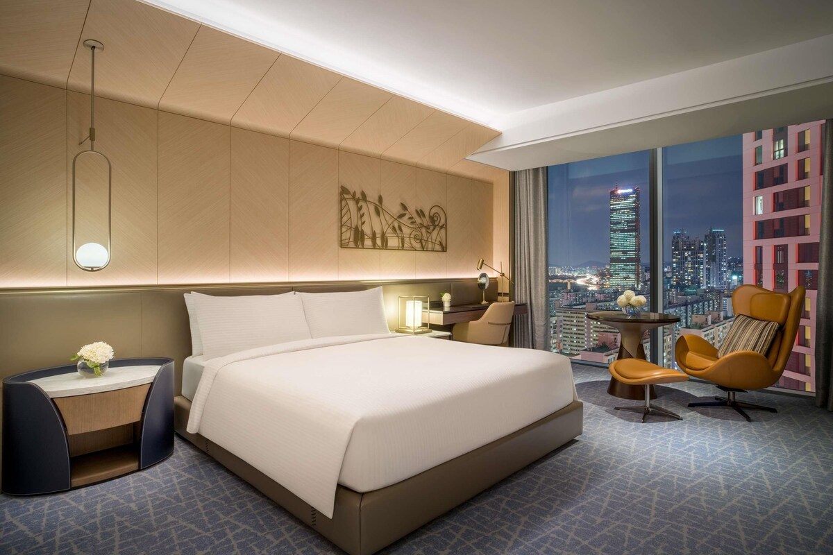 Una habitación de hotel moderna con una cama grande, un escritorio, una silla y vistas a la ciudad.