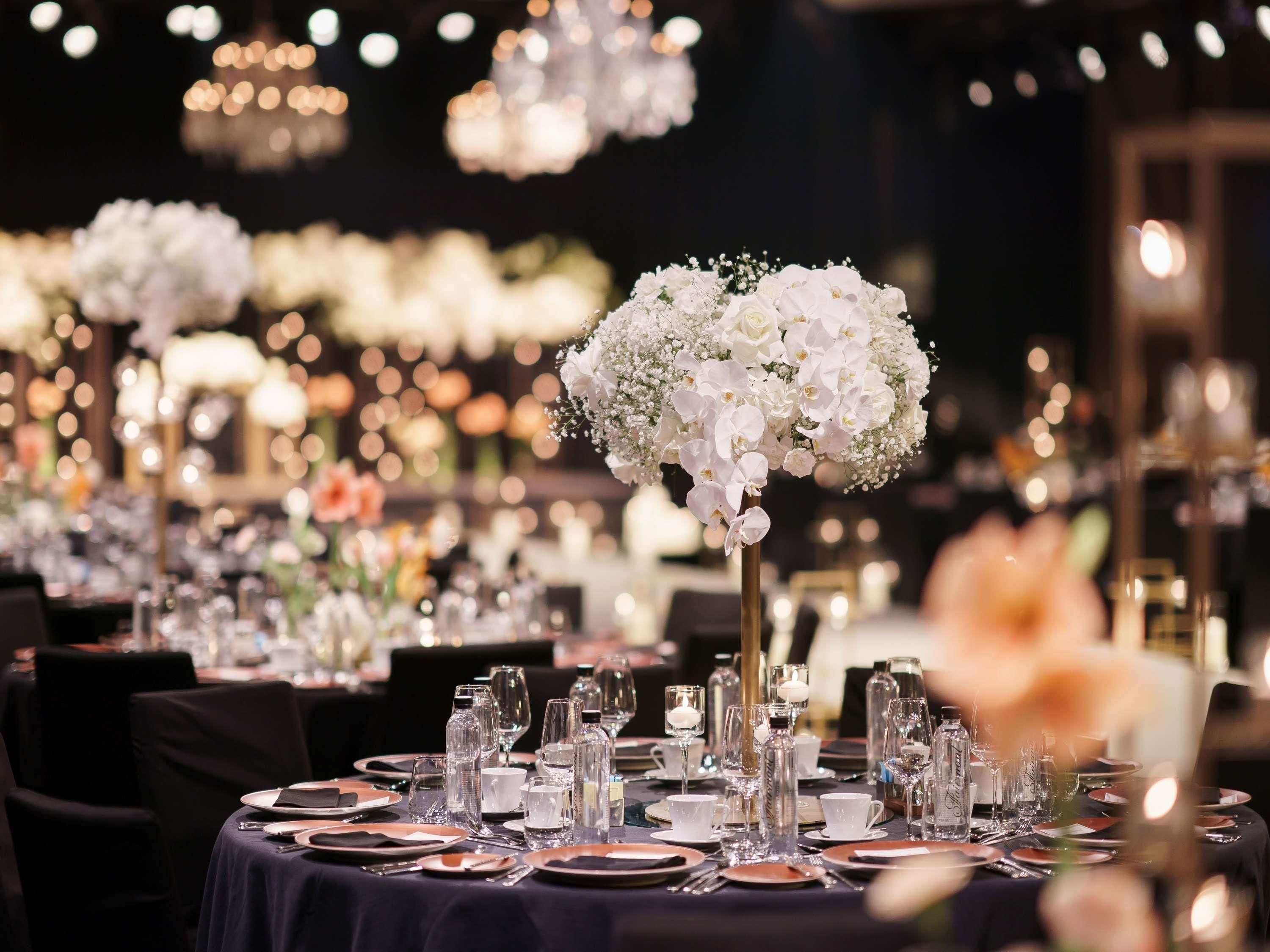 A formal dining setting with tables set for multiple guests, featuring clear glassware, plates, and elegant floral centerpieces.