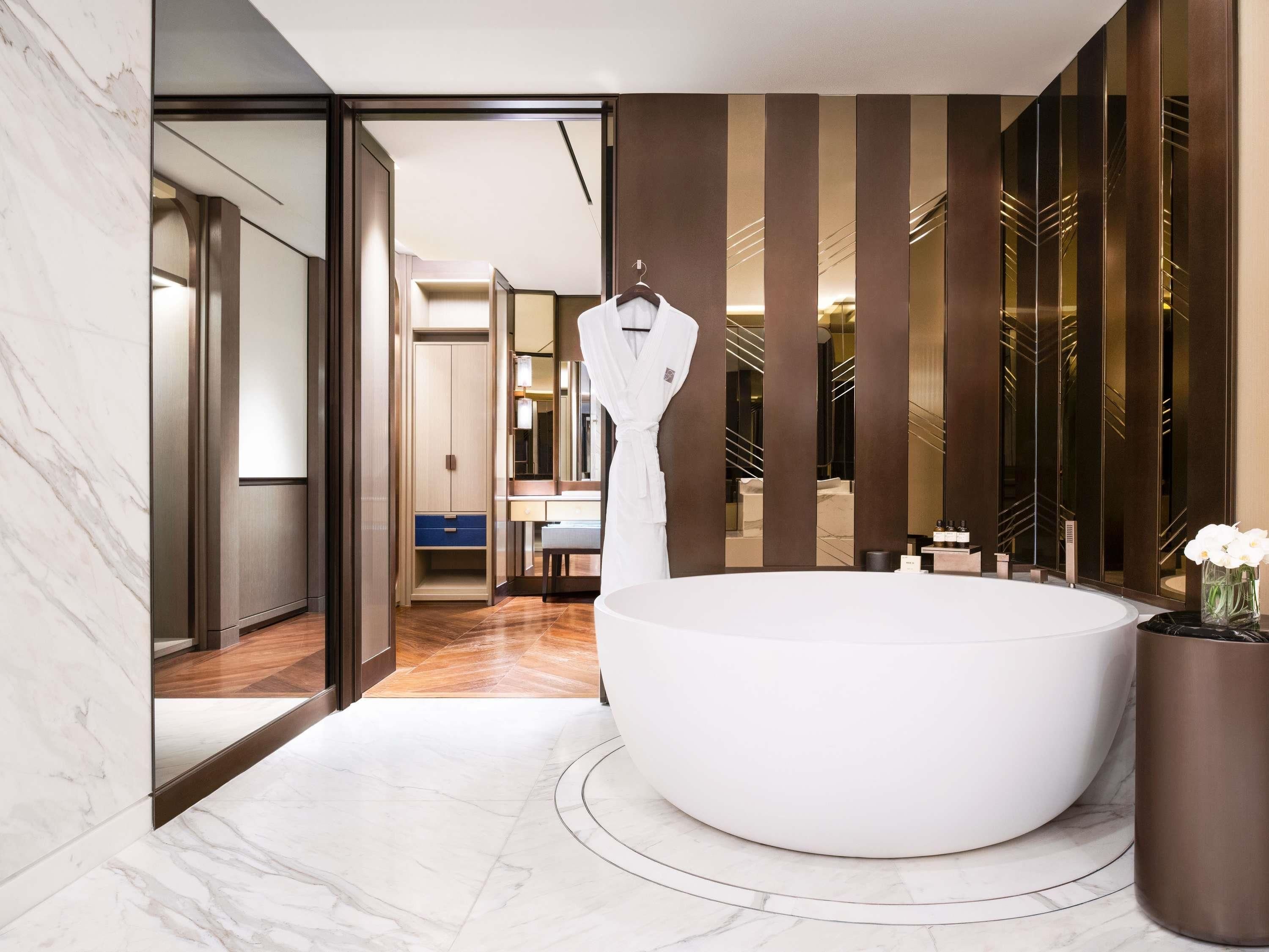 A modern bathroom with a large bathtub, a walk-in closet, and a mirror with a unique design.