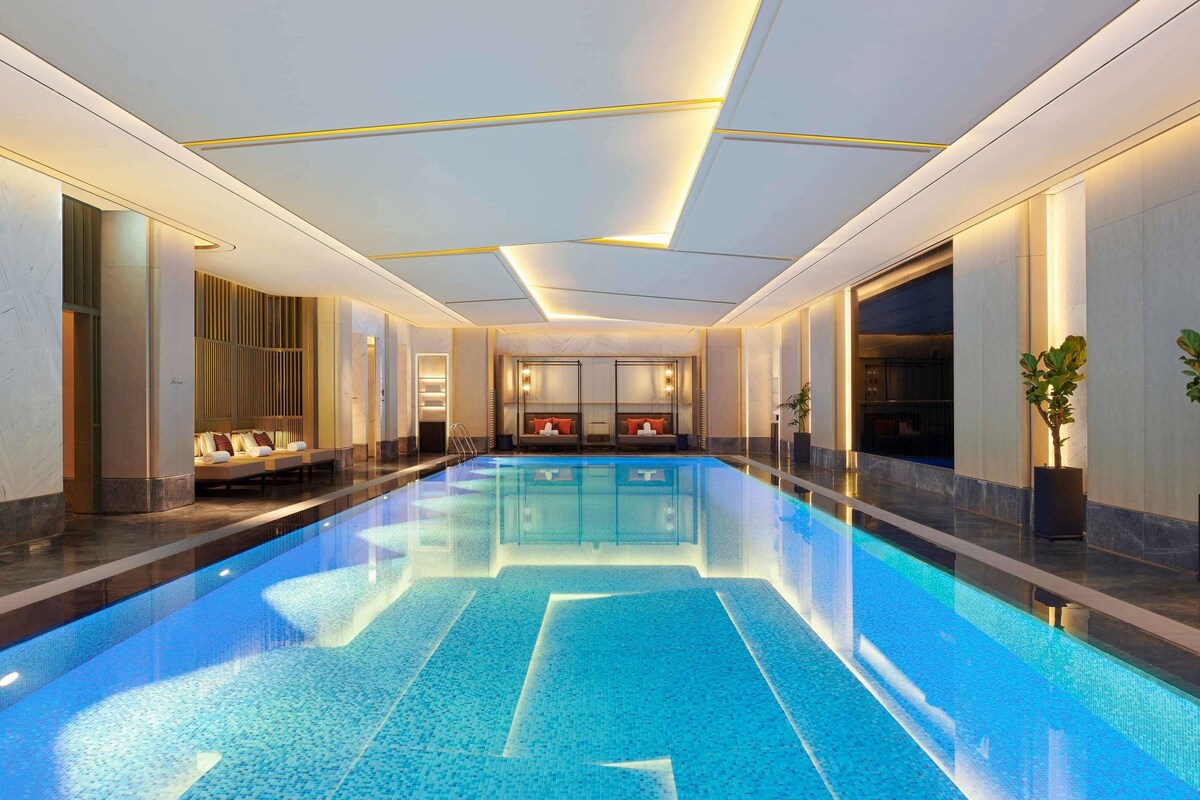 Uma grande piscina interior com design moderno, rodeada por áreas de estar e teto bem iluminado.