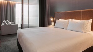 Habitación de hotel moderna con una cama grande, un sofá y vistas a la ciudad a través de amplias ventanas.