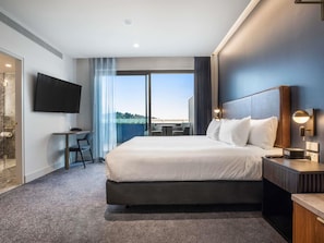 Habitación de hotel con una cama grande, un escritorio con silla, televisor y balcón con vistas.