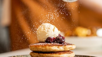 A stack of pancakes with a scoop of ice cream on top, being sprinkled with sugar.