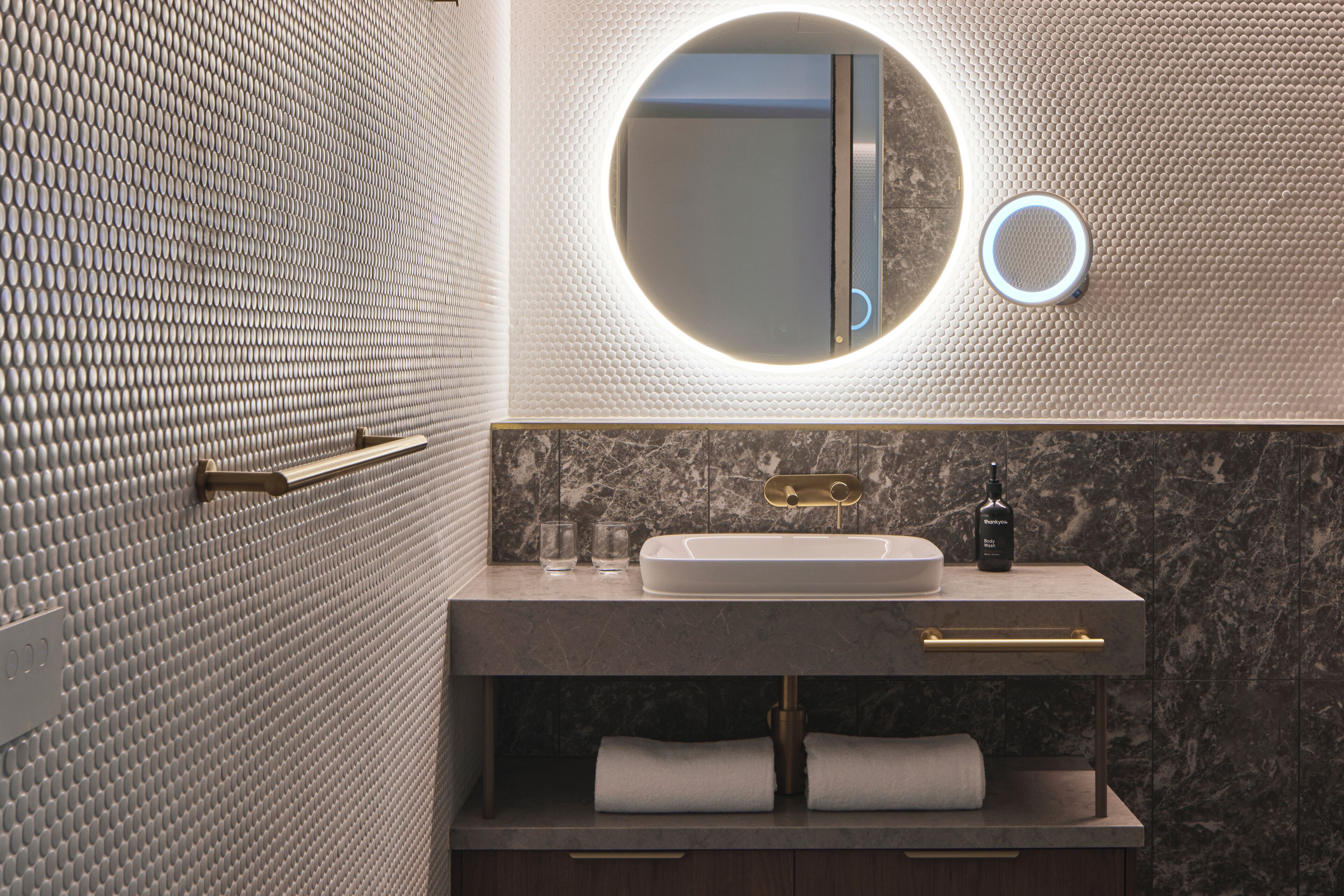Un baño moderno con un espejo redondo, un lavabo y un perchero para toallas.