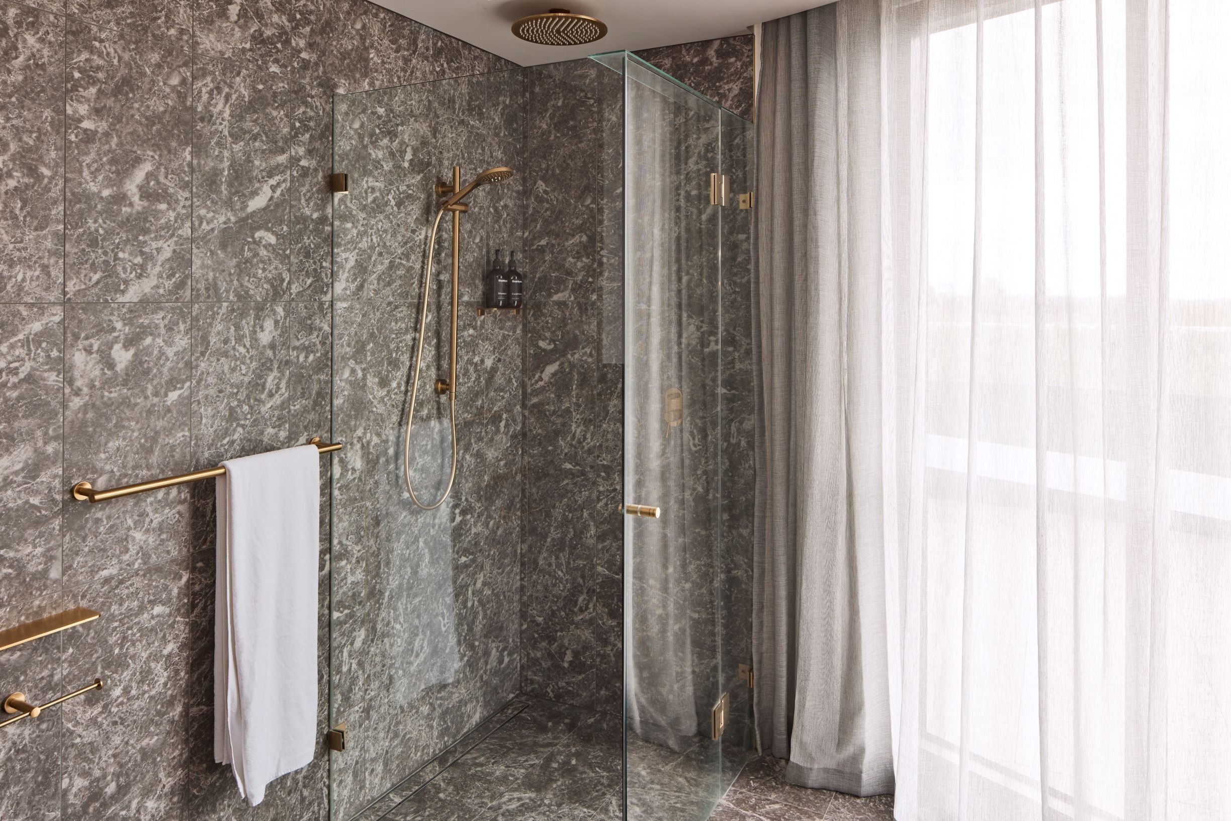 Une salle de bain moderne avec des murs en marbre, une douche en verre et un porte-serviettes.