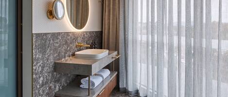 Une salle de bain moderne avec un meuble-lavabo en marbre, un grand miroir et une vue à travers des rideaux transparents.