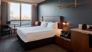Une chambre d’hôtel avec un grand lit, un bureau avec un ordinateur portable, une chaise, une machine à café et une vue sur l’extérieur.