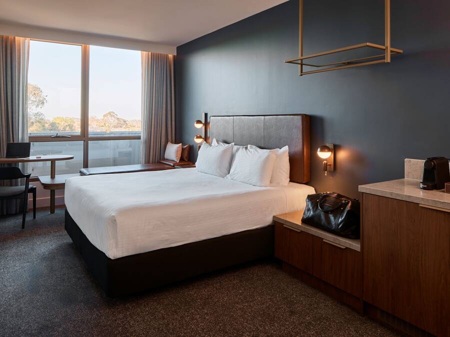 Une chambre d’hôtel avec un grand lit, un bureau avec un ordinateur portable, une chaise, une machine à café et une vue sur l’extérieur.