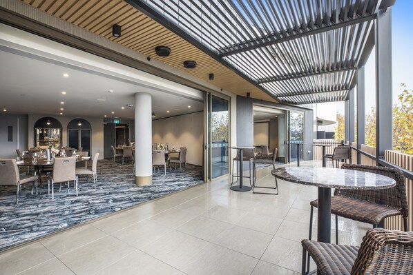 A spacious indoor area with a high ceiling, a patterned floor, and a mix of seating arrangements including round tables and wicker chairs. - Rydges Ringwood (Ringwood)